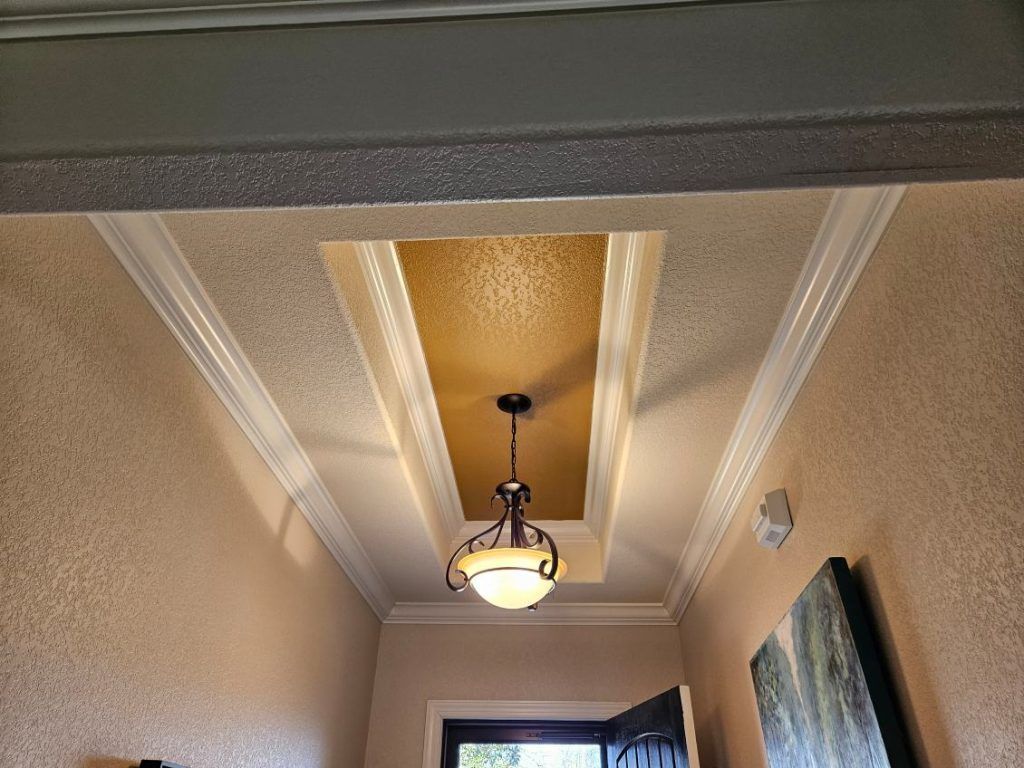 Hallway ceiling with gold painted inset, decorative molding, and hanging light fixture.