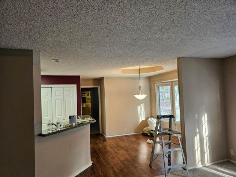 Interior view of a room with walls of beige and a popcorn ceiling; a ladder and chandelier are visible.
