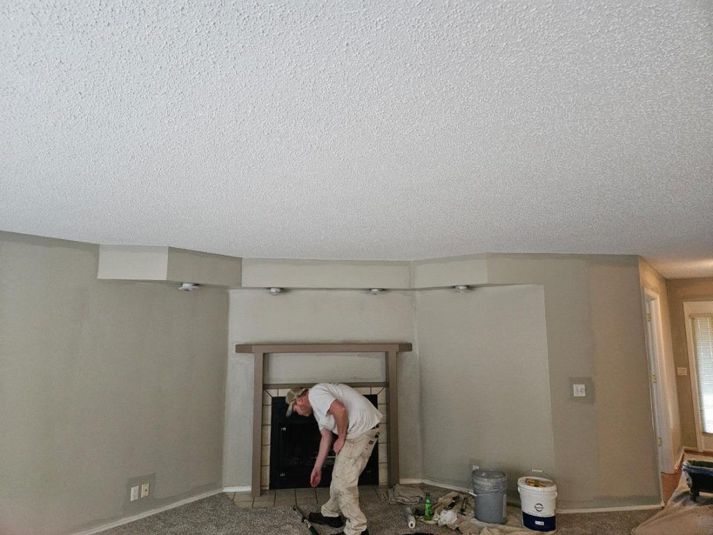 Man painting a room with a fireplace. Light walls and popcorn ceiling.