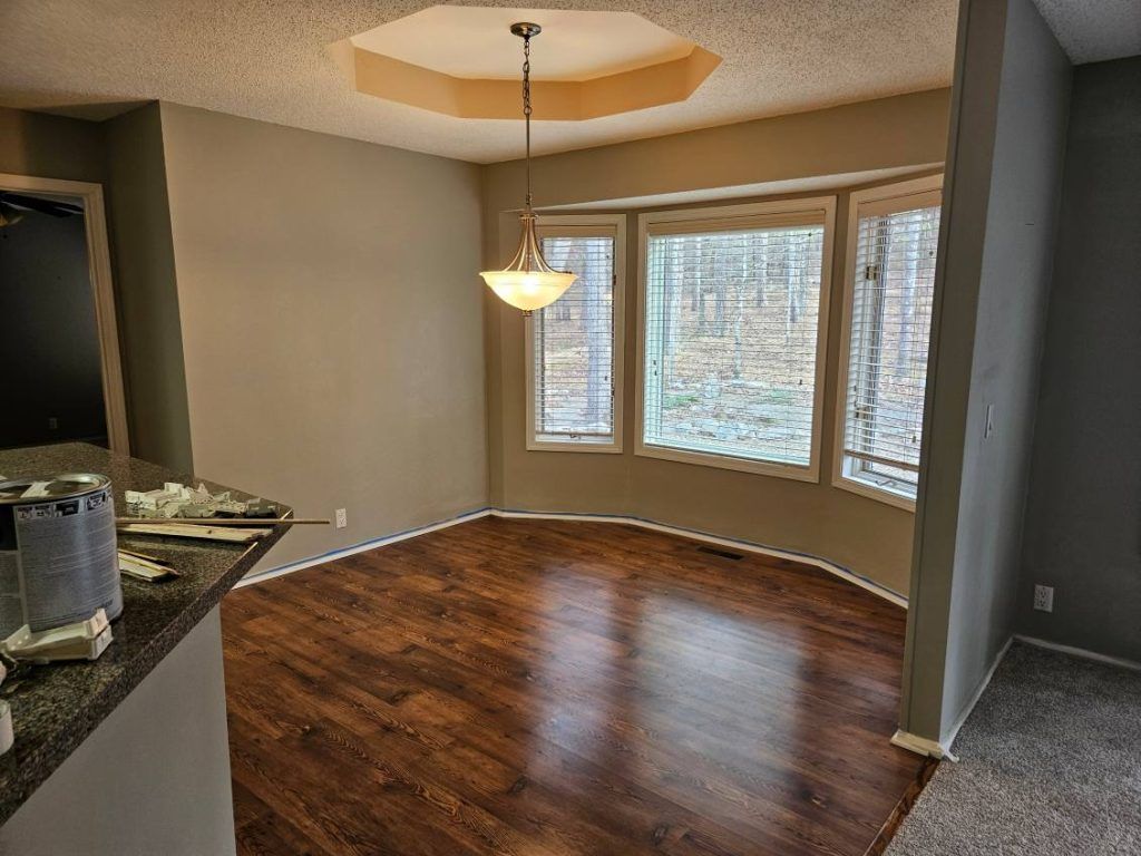 Dining room with dark wood floors, bay window, and a light fixture.