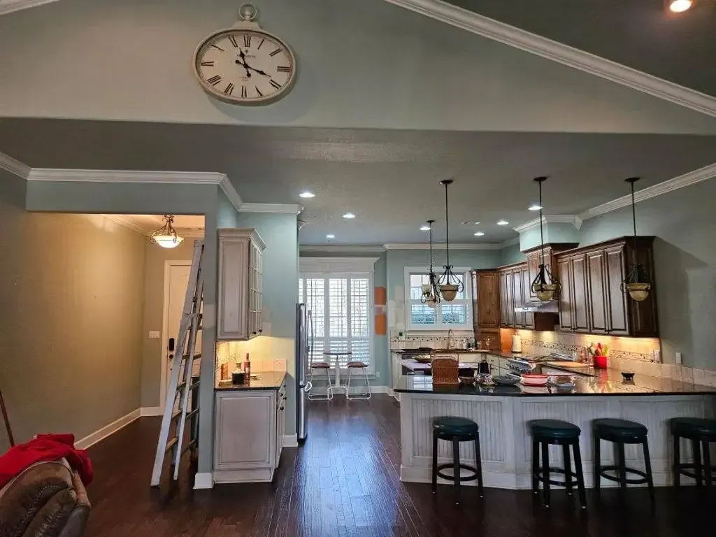 Kitchen with cabinets, island, stools, and a clock on the wall.