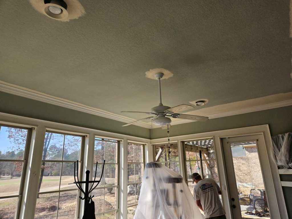 Sunroom with green ceiling, white trim, and ceiling fan. A person in a t-shirt stands in front of a covered easel.
