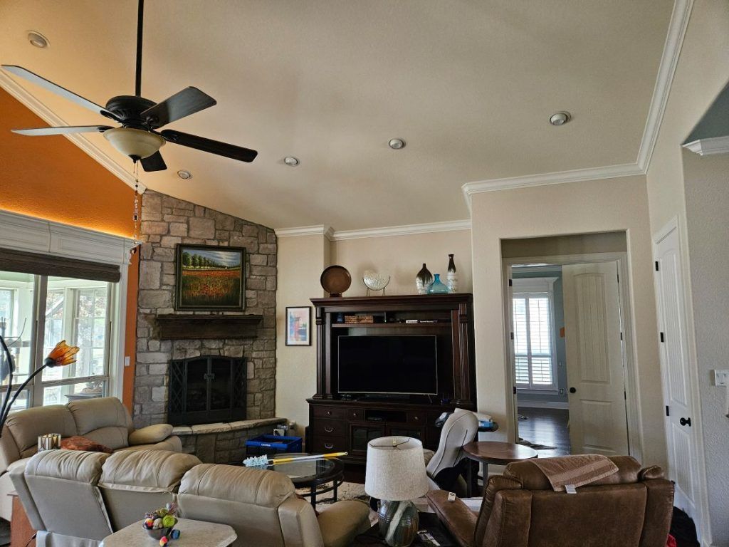 Living room with stone fireplace, TV, and tan sofas. Ceiling fan and light fixtures.