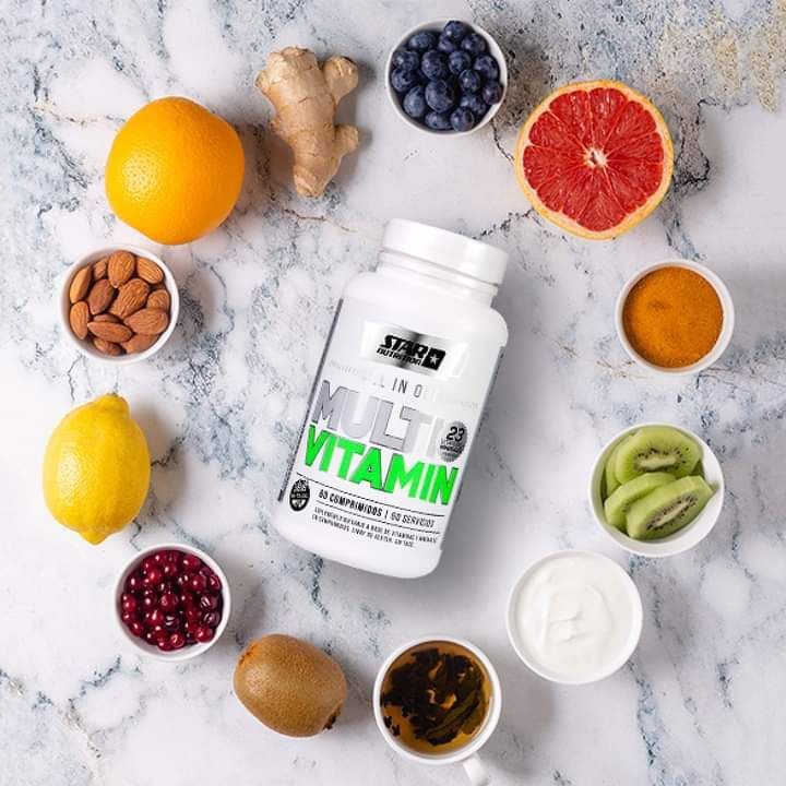 Botella de multivitaminas rodeada de frutas, nueces y yogur sobre una superficie de mármol.