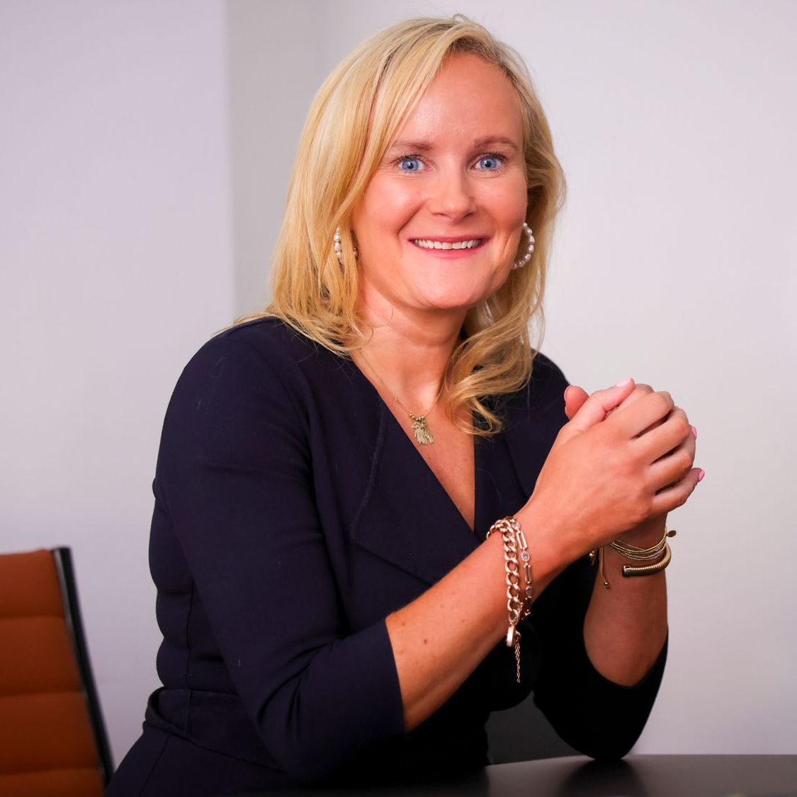 A woman in a blue shirt is smiling with her hands folded