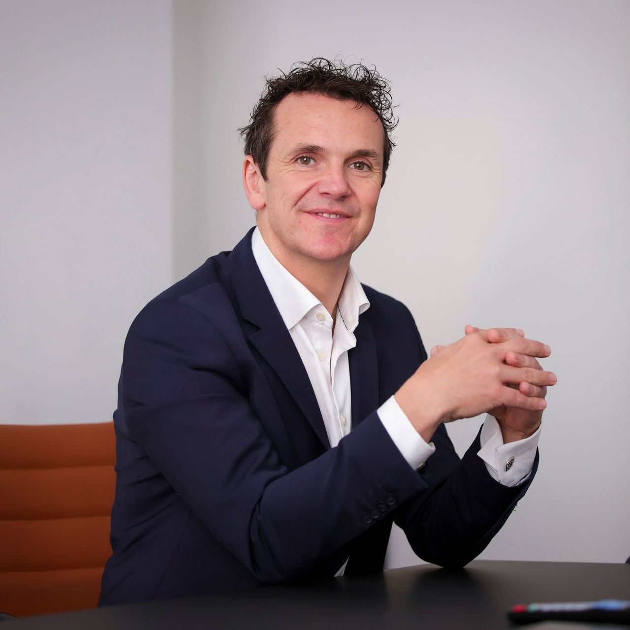 A man in a suit is sitting at a desk with his hands folded