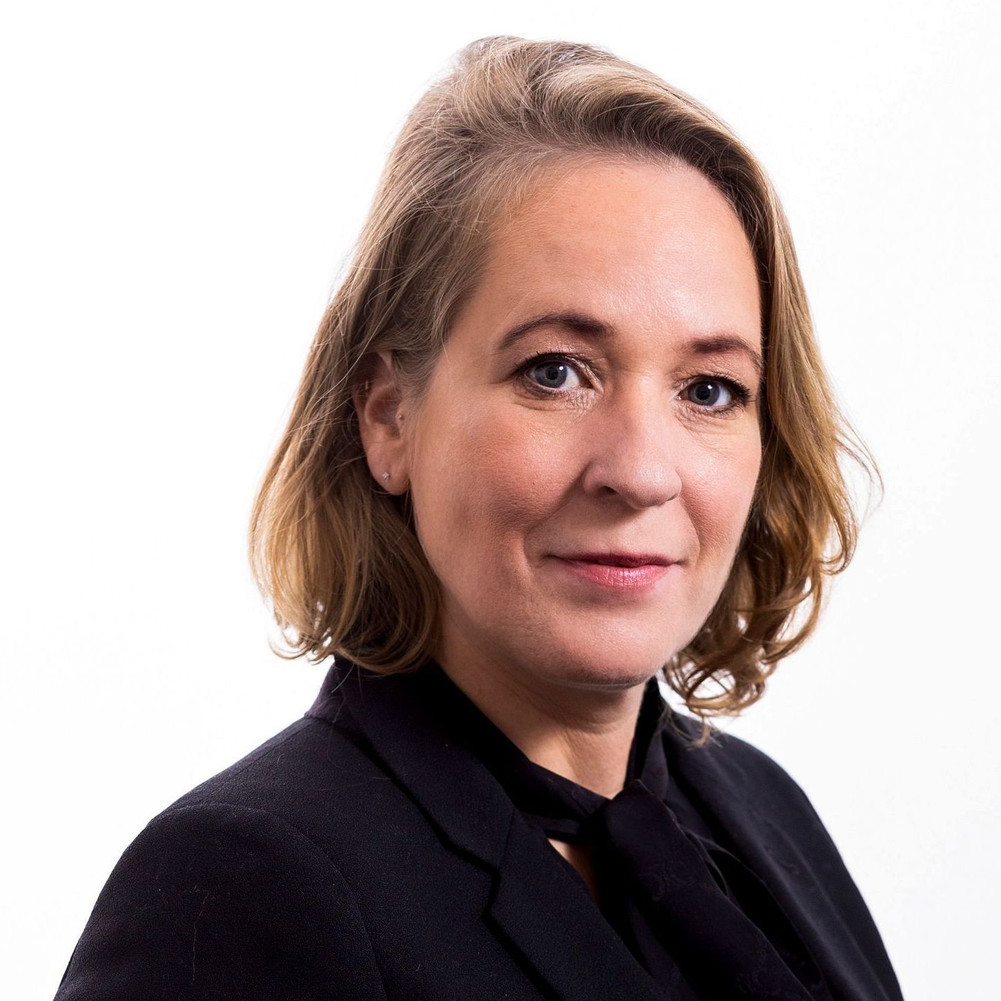 A woman wearing a black jacket and tie smiles for the camera