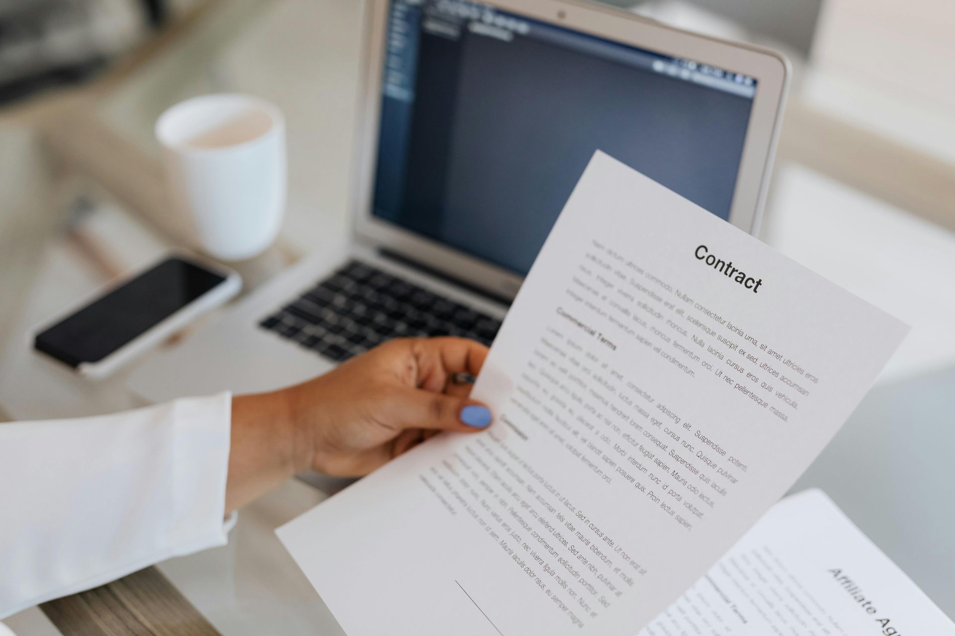 A person is holding a piece of paper in front of a laptop computer.