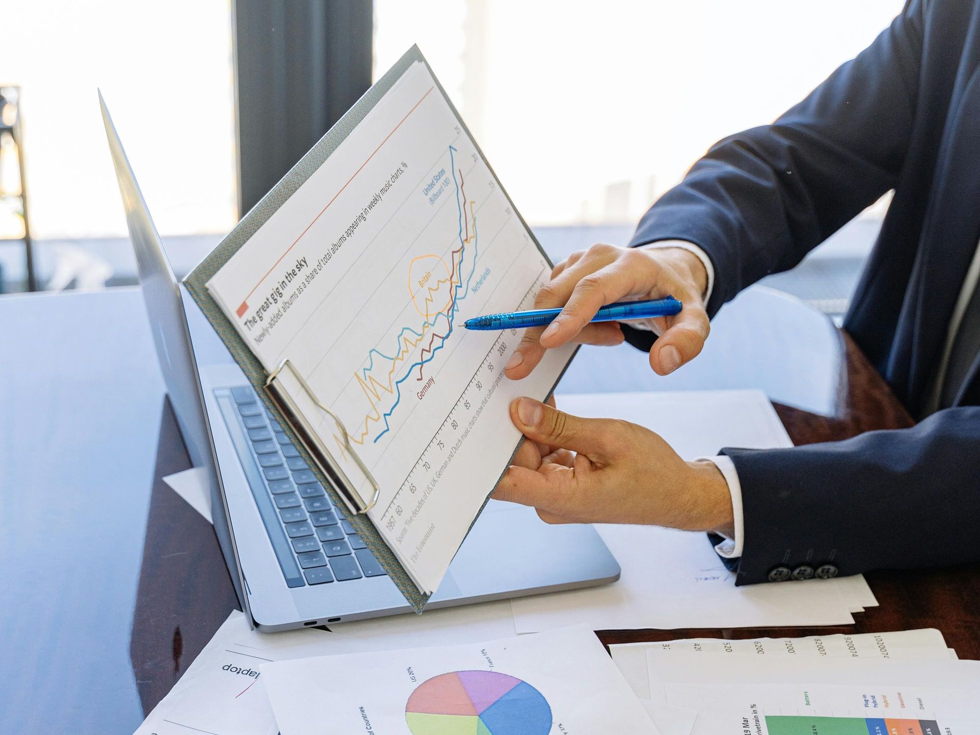 A man is pointing at a graph on a piece of paper in front of a laptop.