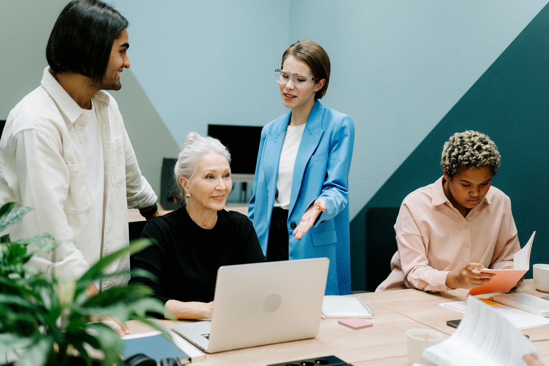 A group of people are standing around a table with a laptop.