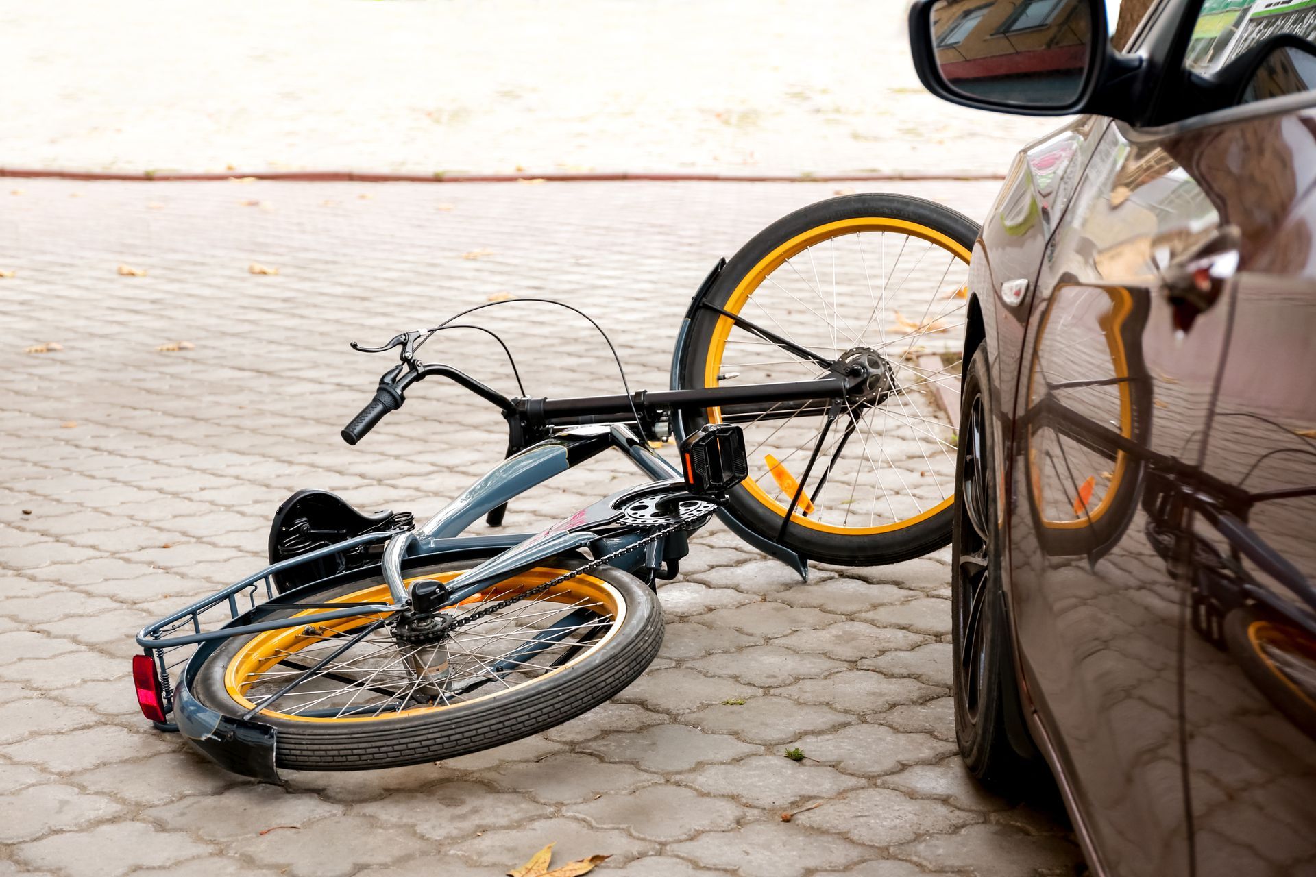 A bicycle lying on paved ground next to the side of a car.
