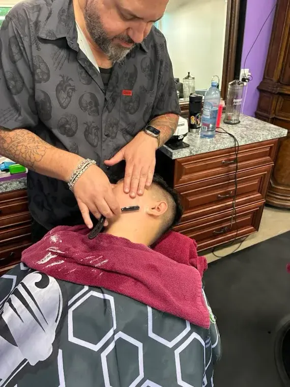 A barber using a straight razor to shave a customer's cheek in a salon setting.