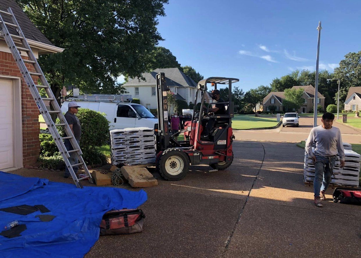 Workers unloading shingles with a forklift near a house; a woman walks nearby.