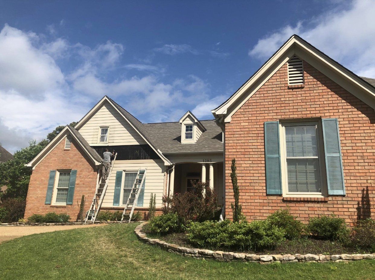 House being painted; brick facade, tan siding, teal shutters, ladders, man on ladder.