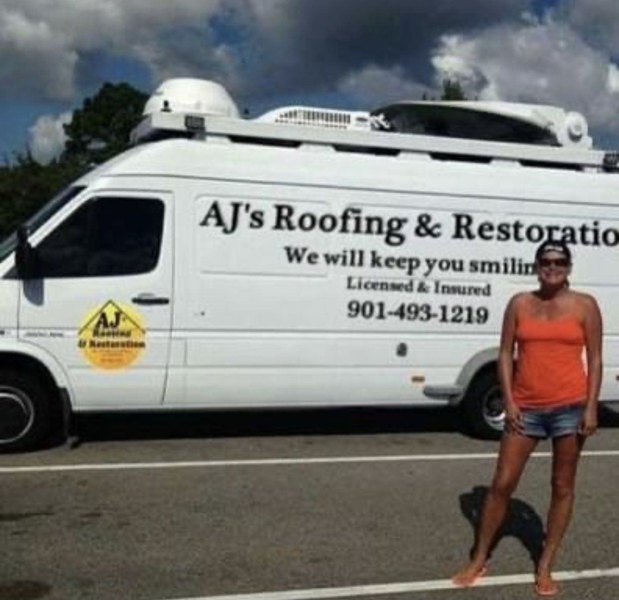 Woman standing by AJ's Roofing van. Orange top, denim shorts, sunny day.