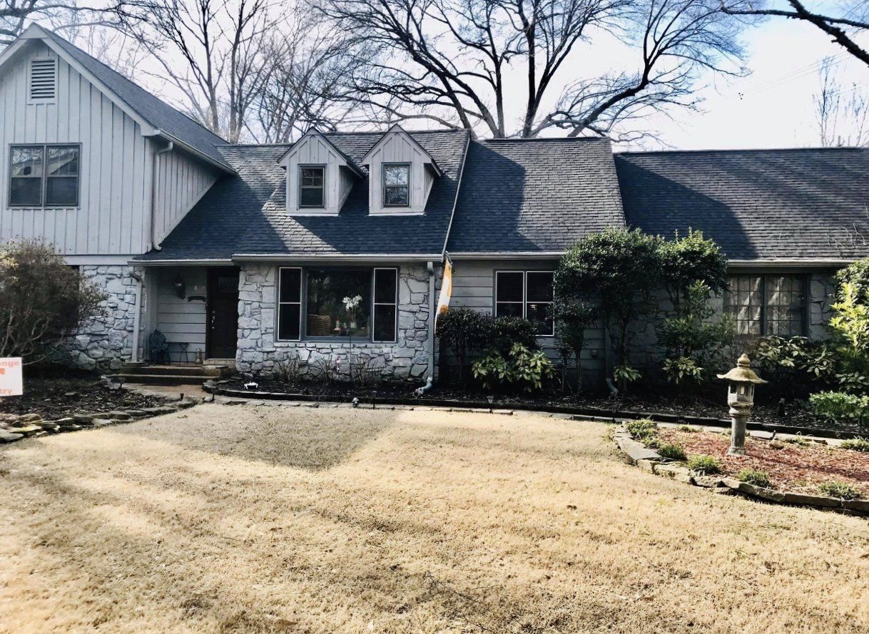 Gray house with stone facade and tan lawn.