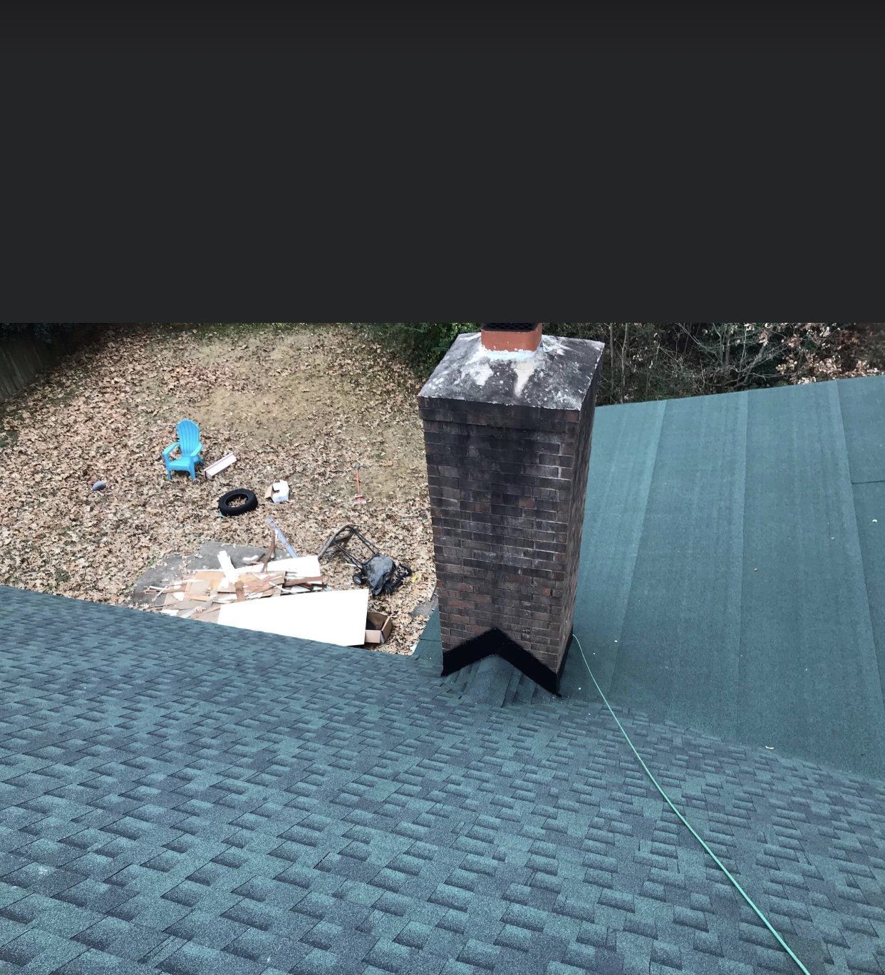 Brick chimney on a green shingled roof. Backyard in the background.