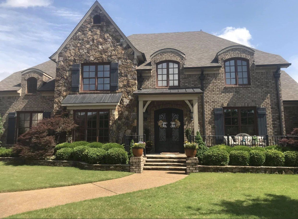 Stone house with blue shutters, a front porch, and a walkway on a sunny day.