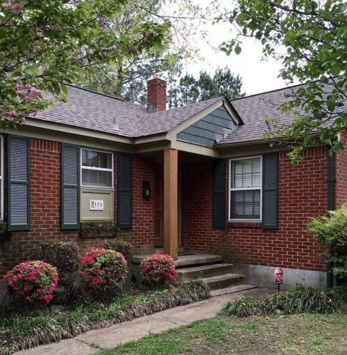 Red brick house with a gray roof, dark green shutters, and a concrete walkway.