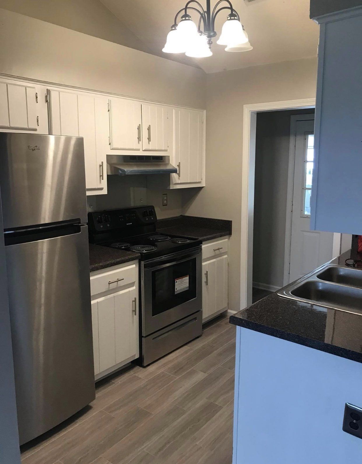 White kitchen with stainless steel appliances, dark countertops, and light wood-look flooring.