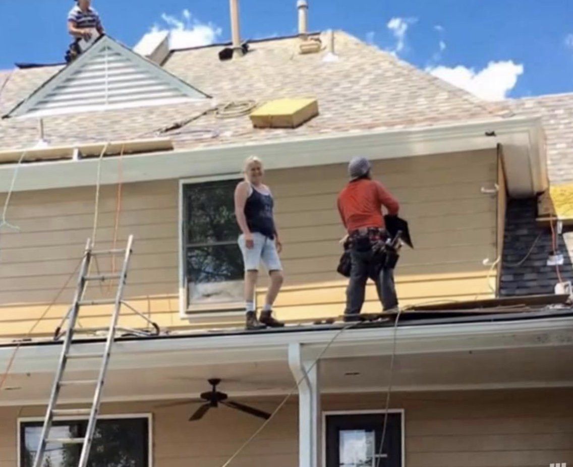 Construction workers on a house roof installing siding. One man in harness, another on the roof, one at the top of a ladder.
