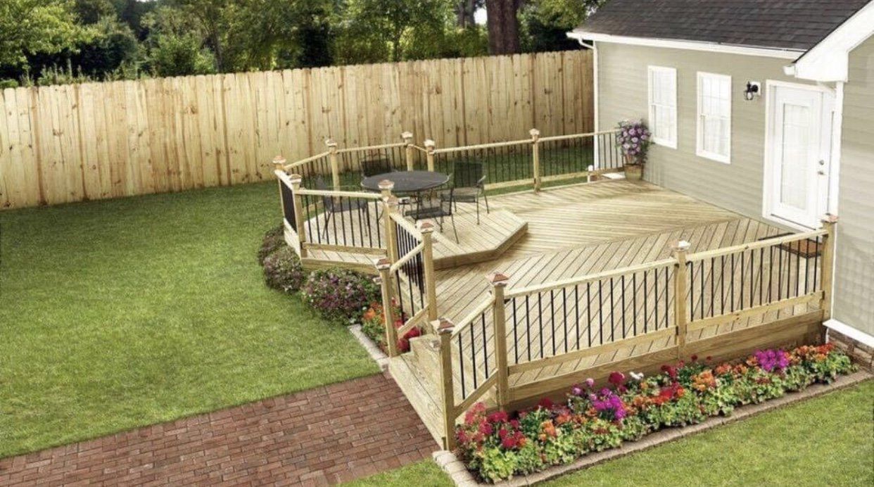 Wooden deck with railing and furniture, adjacent to a house and a fenced yard.