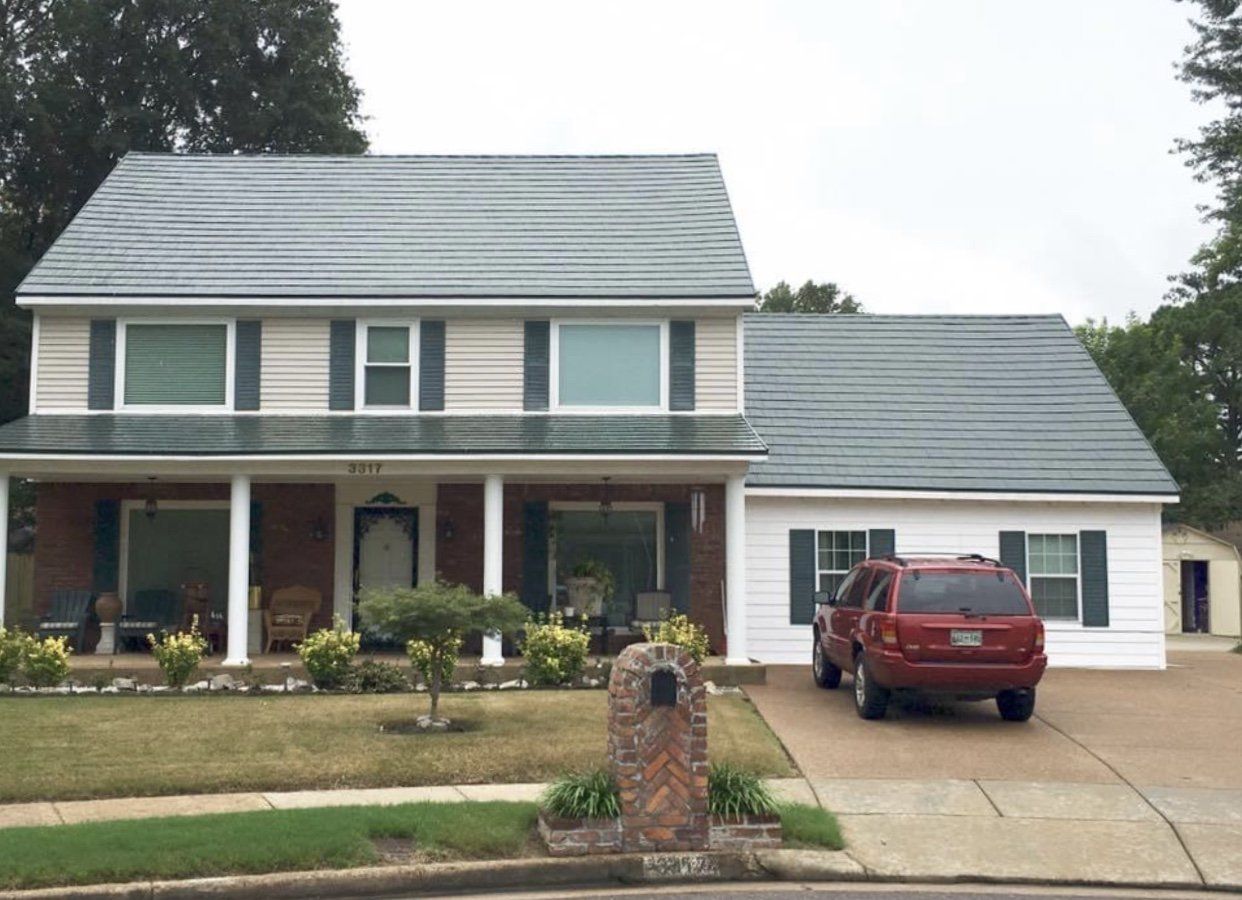 Two-story house with a red SUV in the driveway. Gray roof, white siding, and brick mailbox.