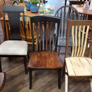 Assorted wooden dining chairs displayed in a furniture store, including dark, gray, and light finishes.