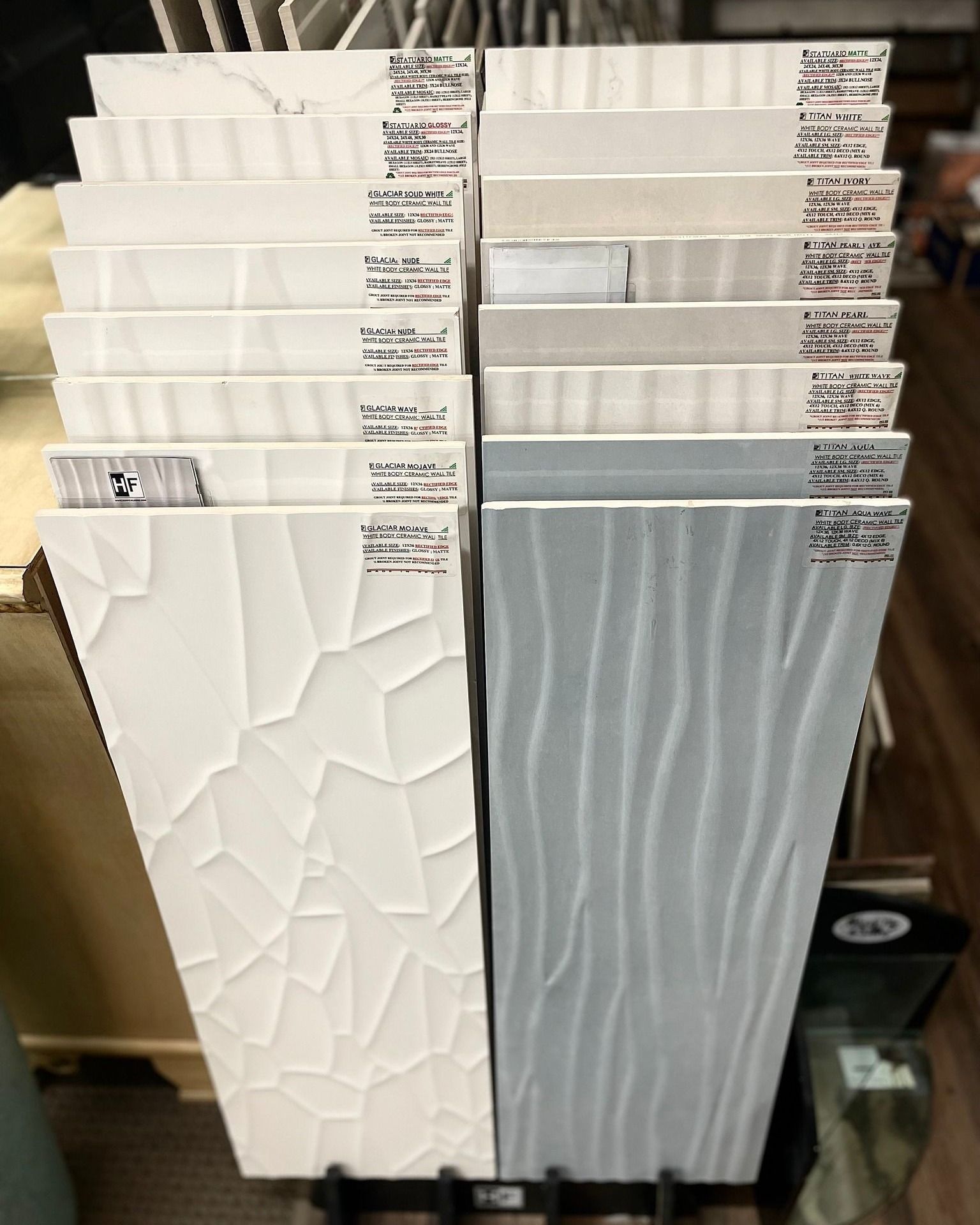 Stacked white and gray textured wall tiles with labels on top, displayed in a showroom