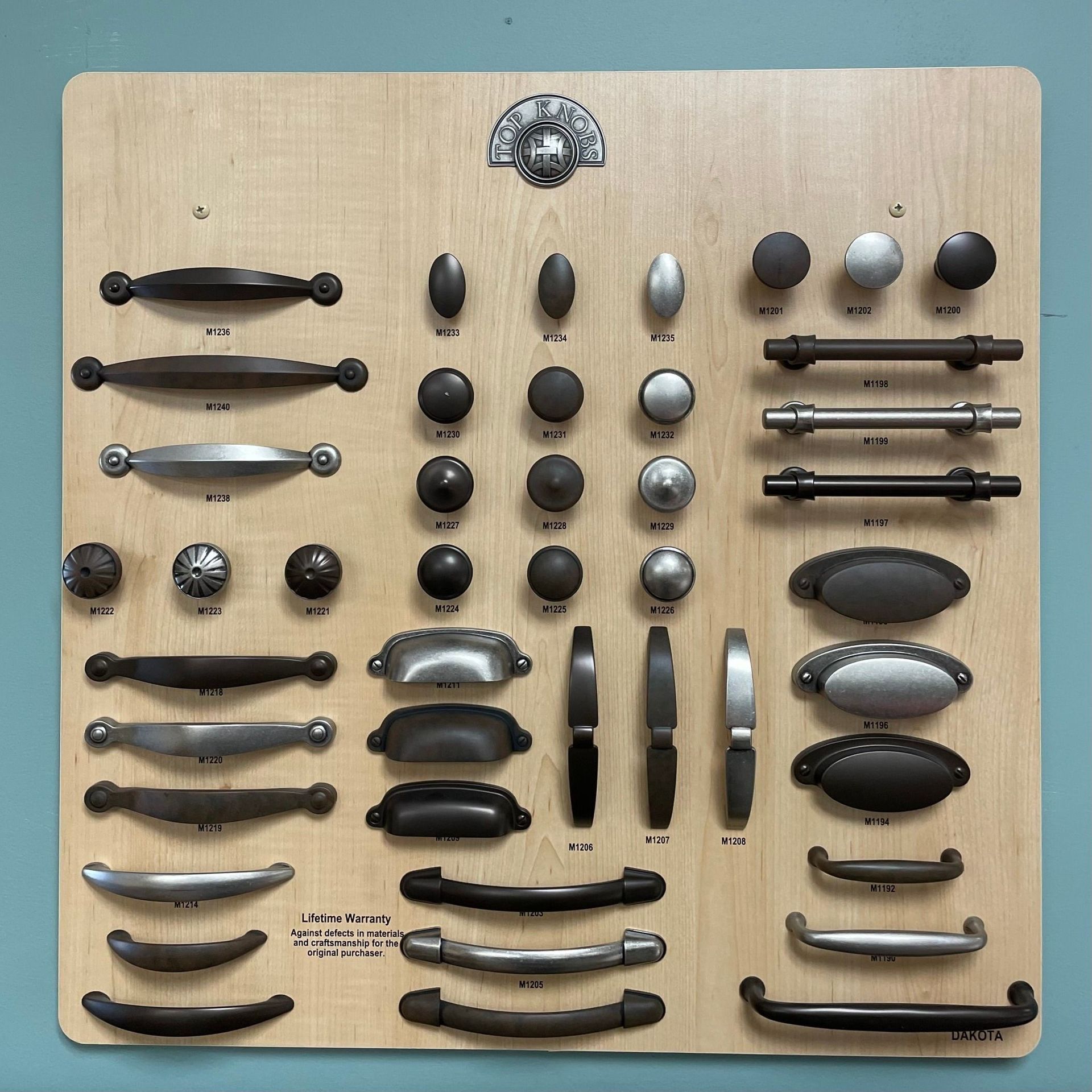 Assorted black, silver, and gray drawer handles and pulls arranged on a wooden board.