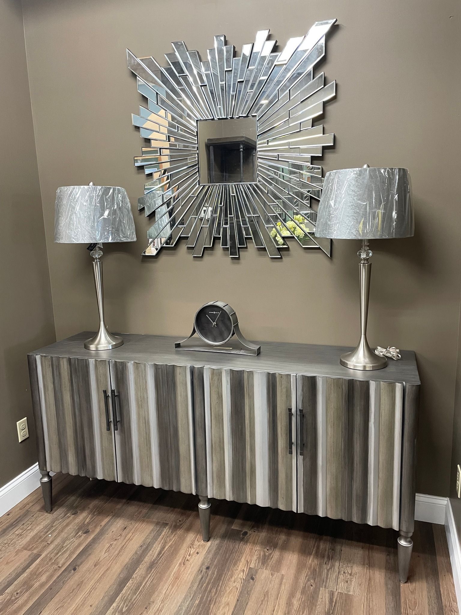 Modern console table with silver lamps and a decorative mirror in a room with wood flooring