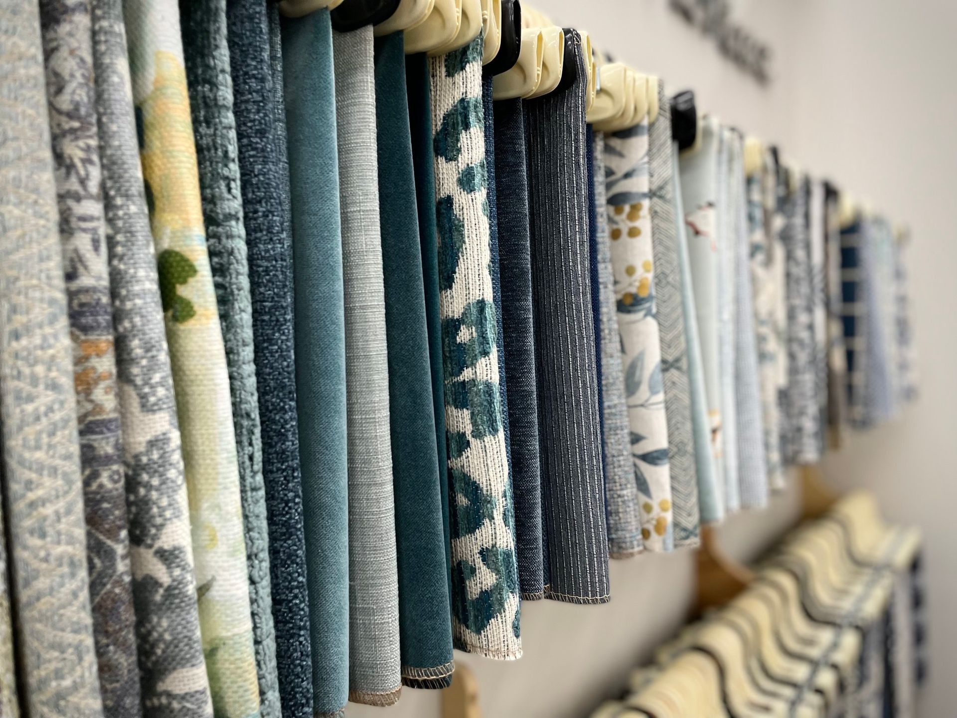 Rolls of patterned fabric hanging on display, with blue, gray, and beige textiles arranged in rows.