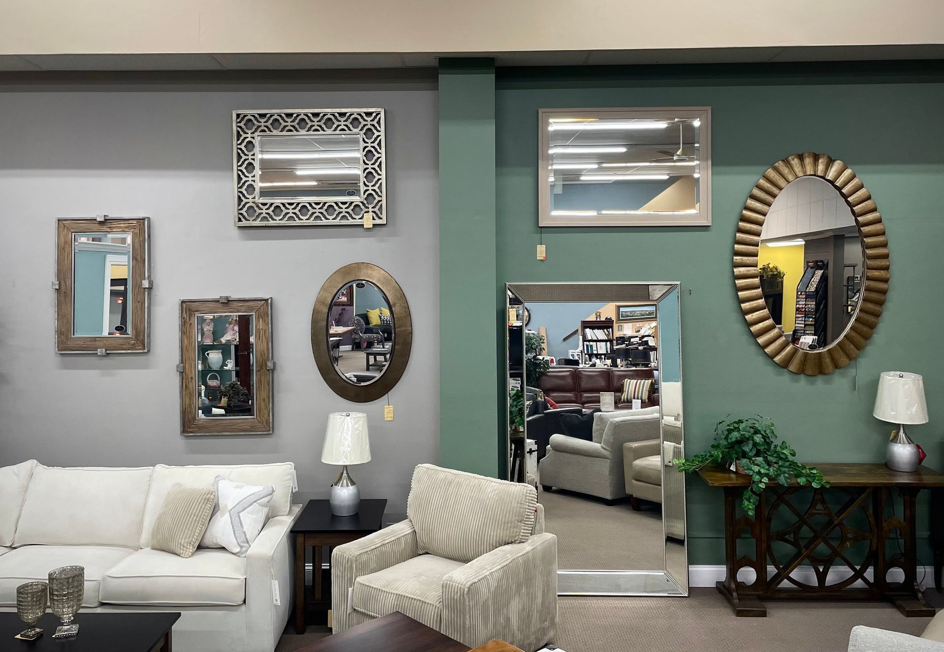 Living room with eclectic framed mirrors, teal accent wall, white sofa, and patterned armchair