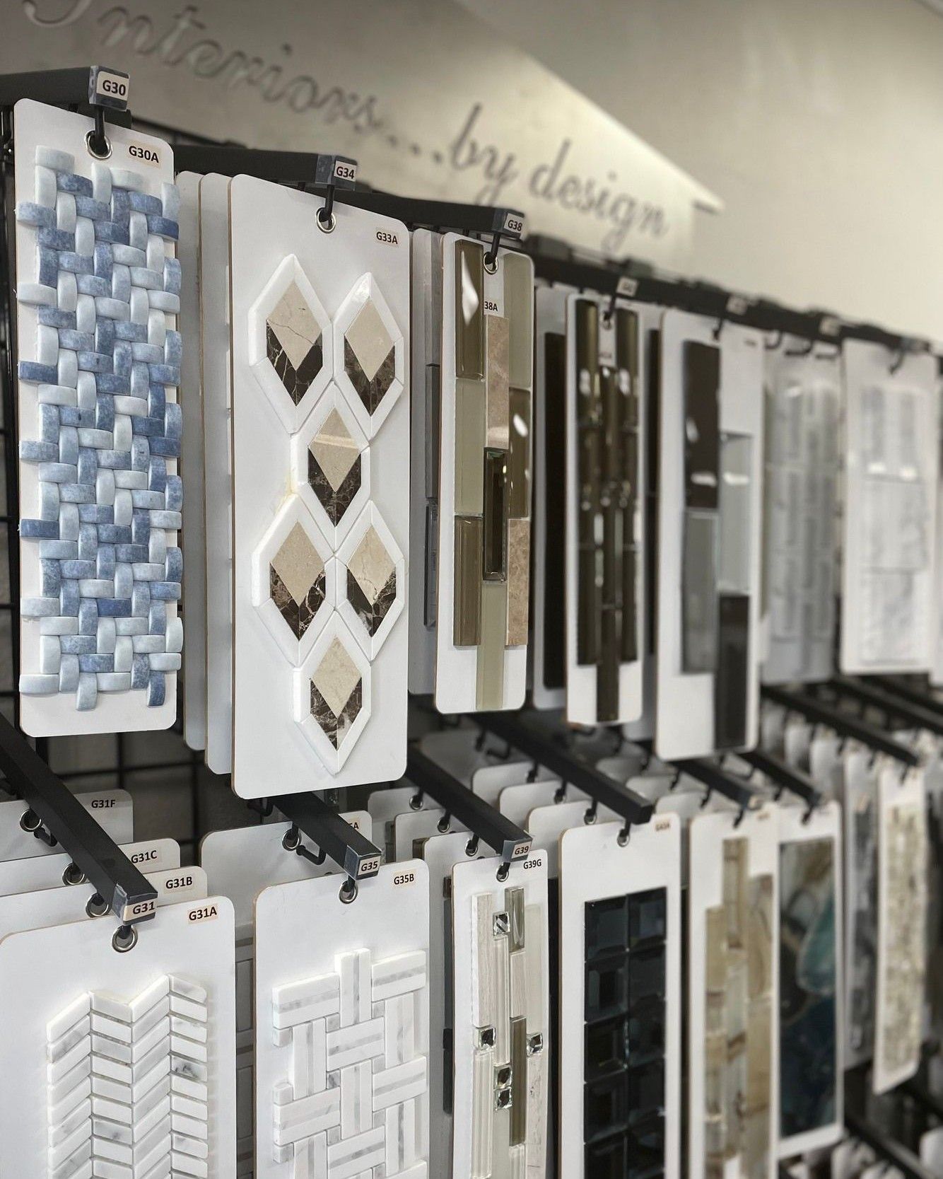 Display of hanging decorative tile samples in white, gray, and black on a showroom wall