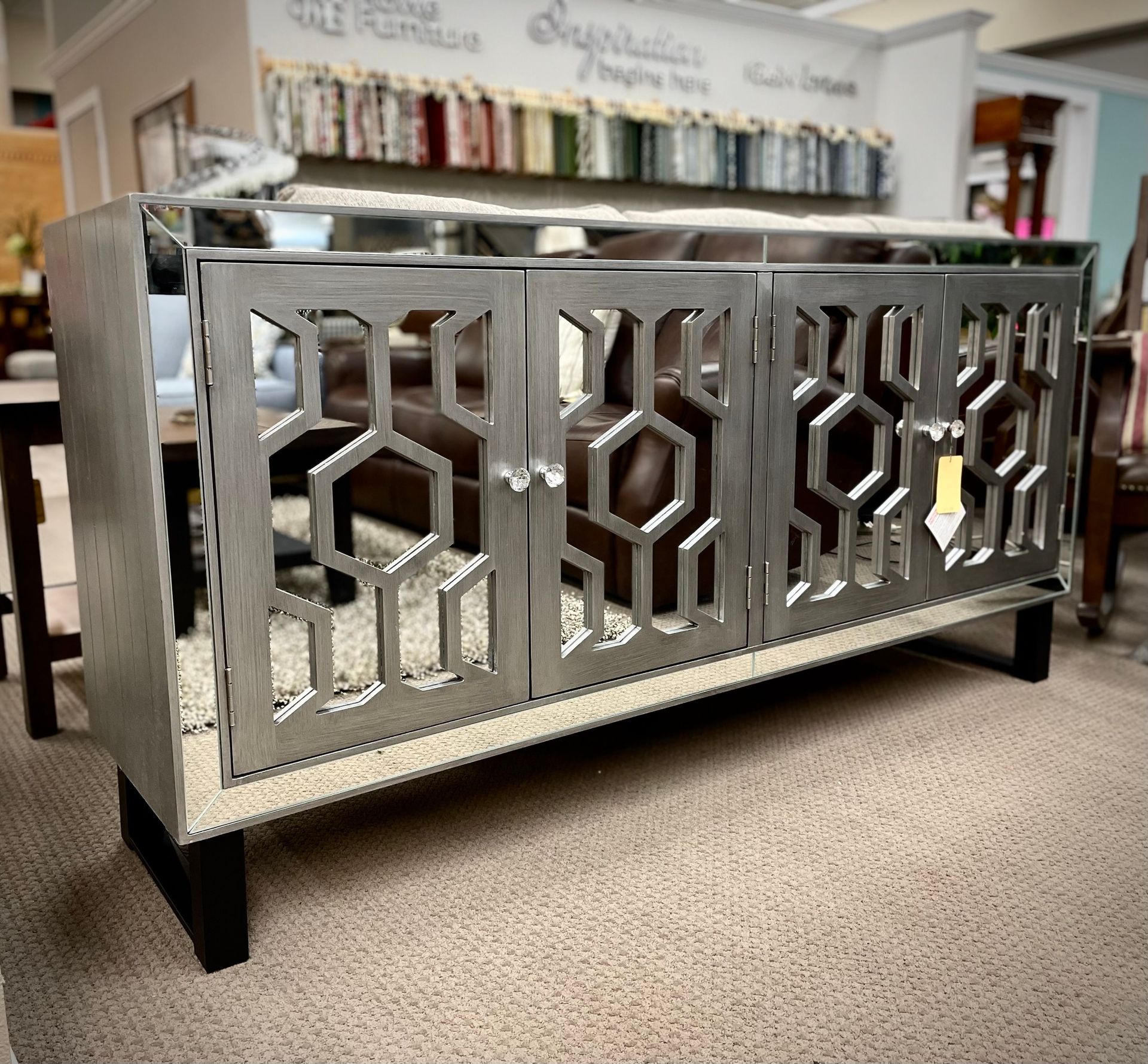 Mirrored chrome sideboard with geometric cutout doors on a carpeted floor in a showroom
