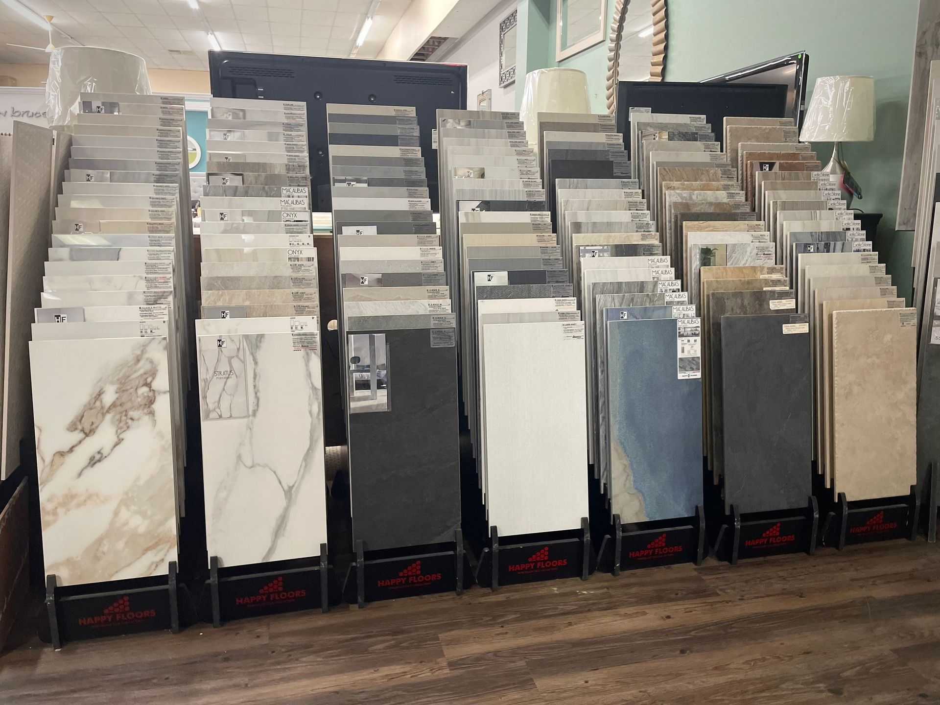 Tile display racks in a showroom aisle, with large sample slabs in white, gray, and beige.