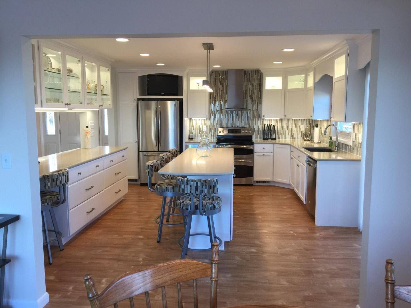 Bright kitchen with white cabinets, stainless steel fridge, island stools, and hardwood floors