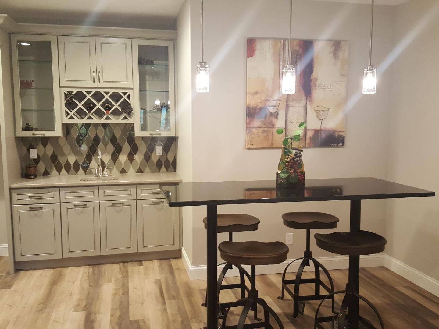 Modern kitchen with white cabinets, mosaic backsplash, and a dark island with three stools under pendant lights