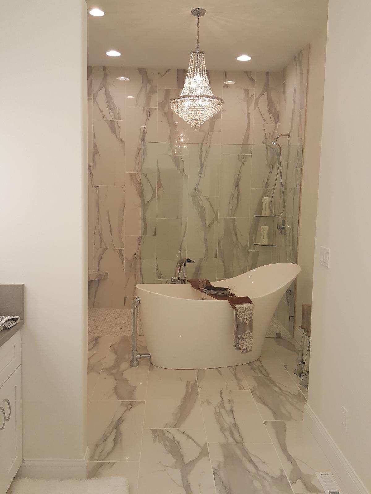 Luxury marble bathroom with crystal chandelier and freestanding tub under a glass shower wall