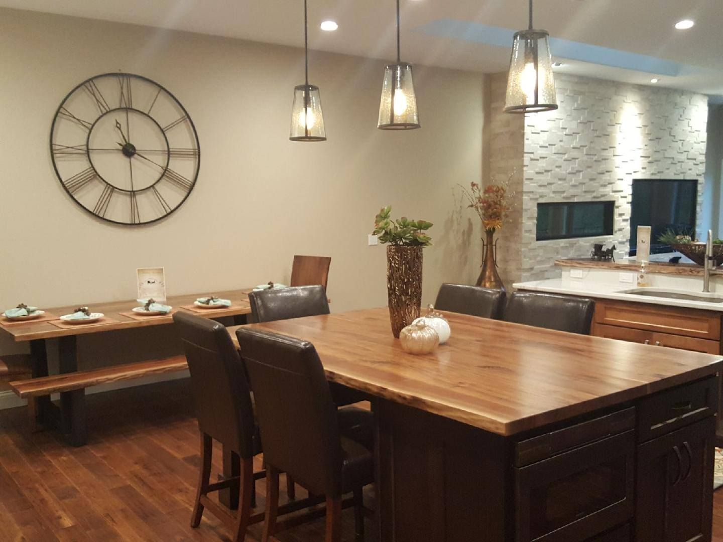 Modern dining room with wooden tables, leather chairs, pendant lights, and a large wall clock