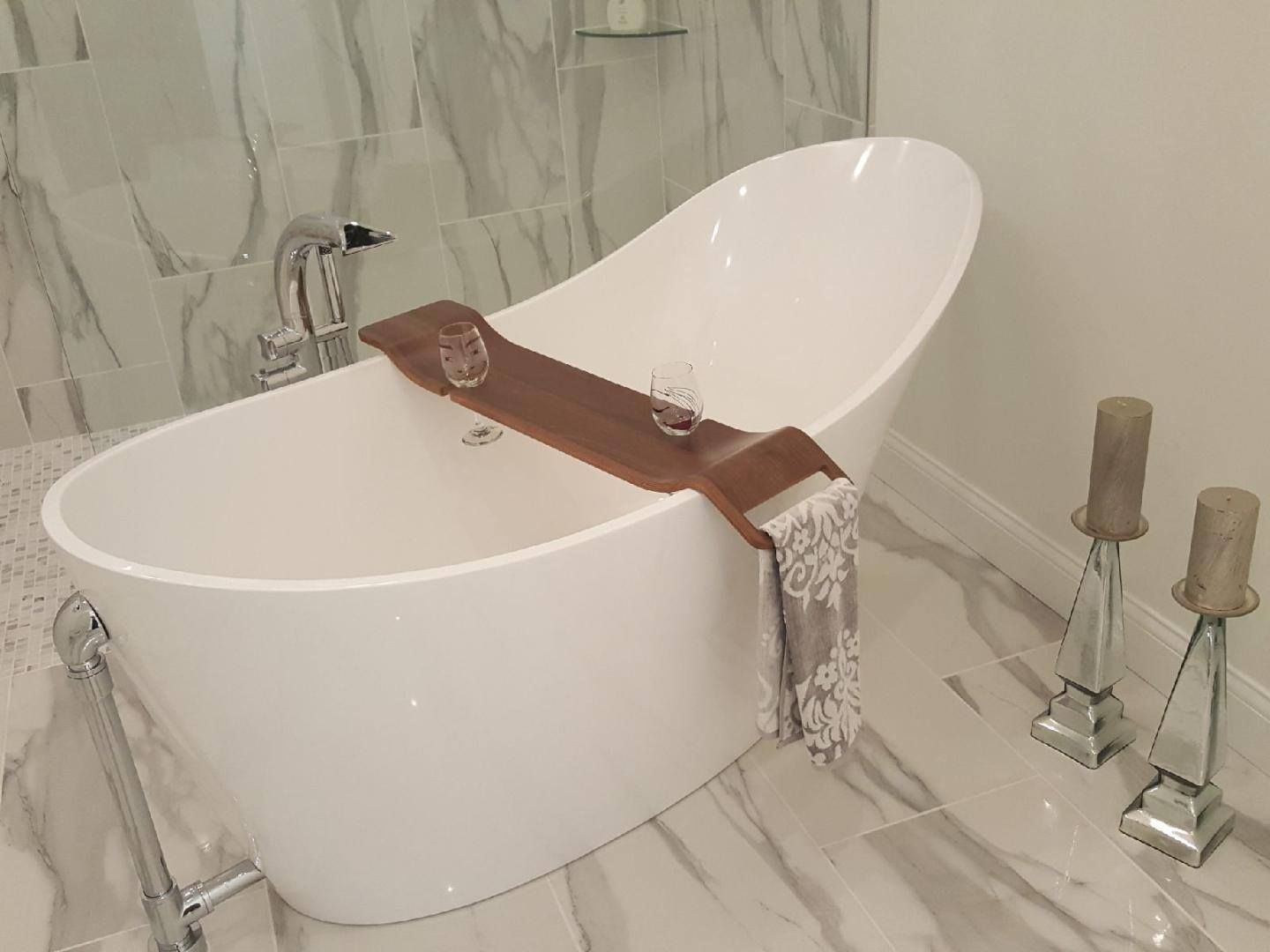 Modern white freestanding bathtub with brown towel, in a marble-tiled bathroom