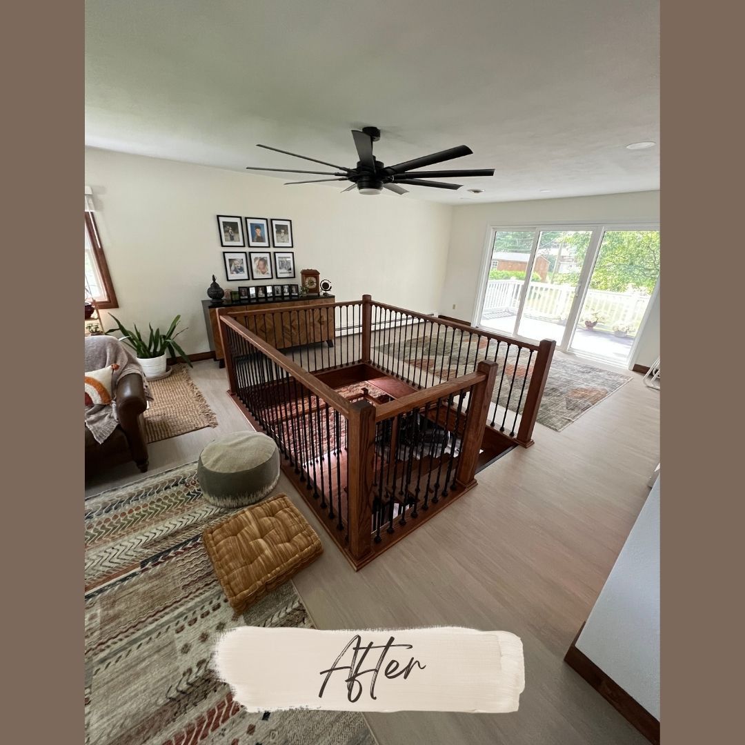 After: open upstairs landing with brown railings, black ceiling fan, patterned rug, and large windows.