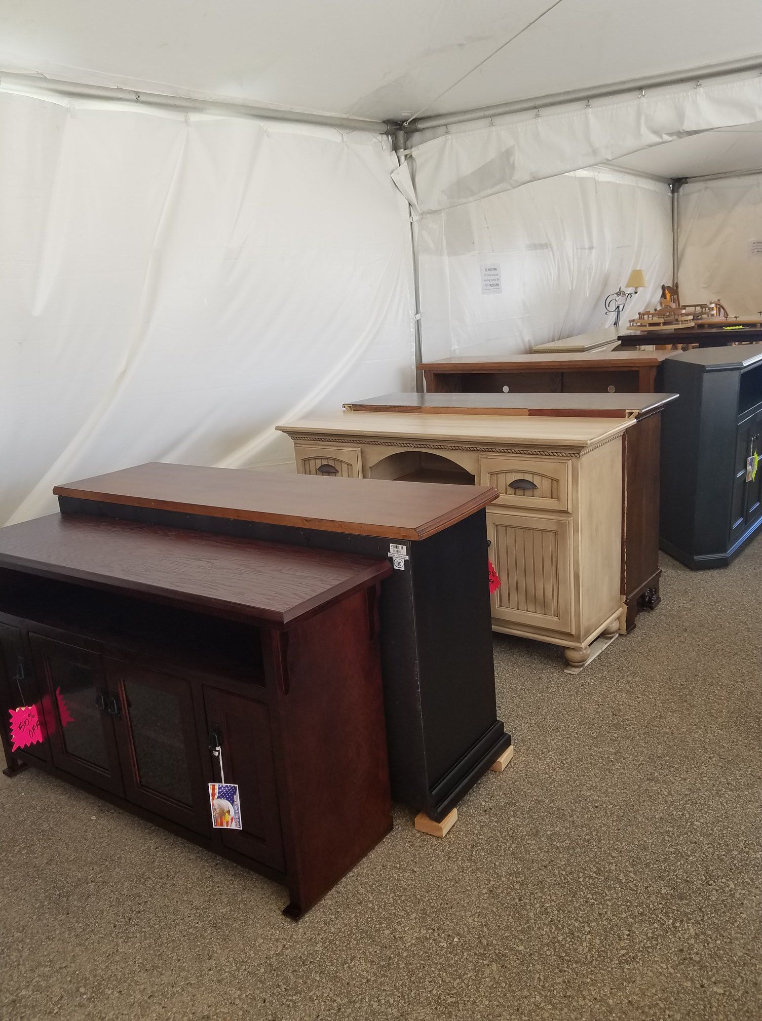 Several wooden office cabinets and desks lined up inside a white tent-like storage space.