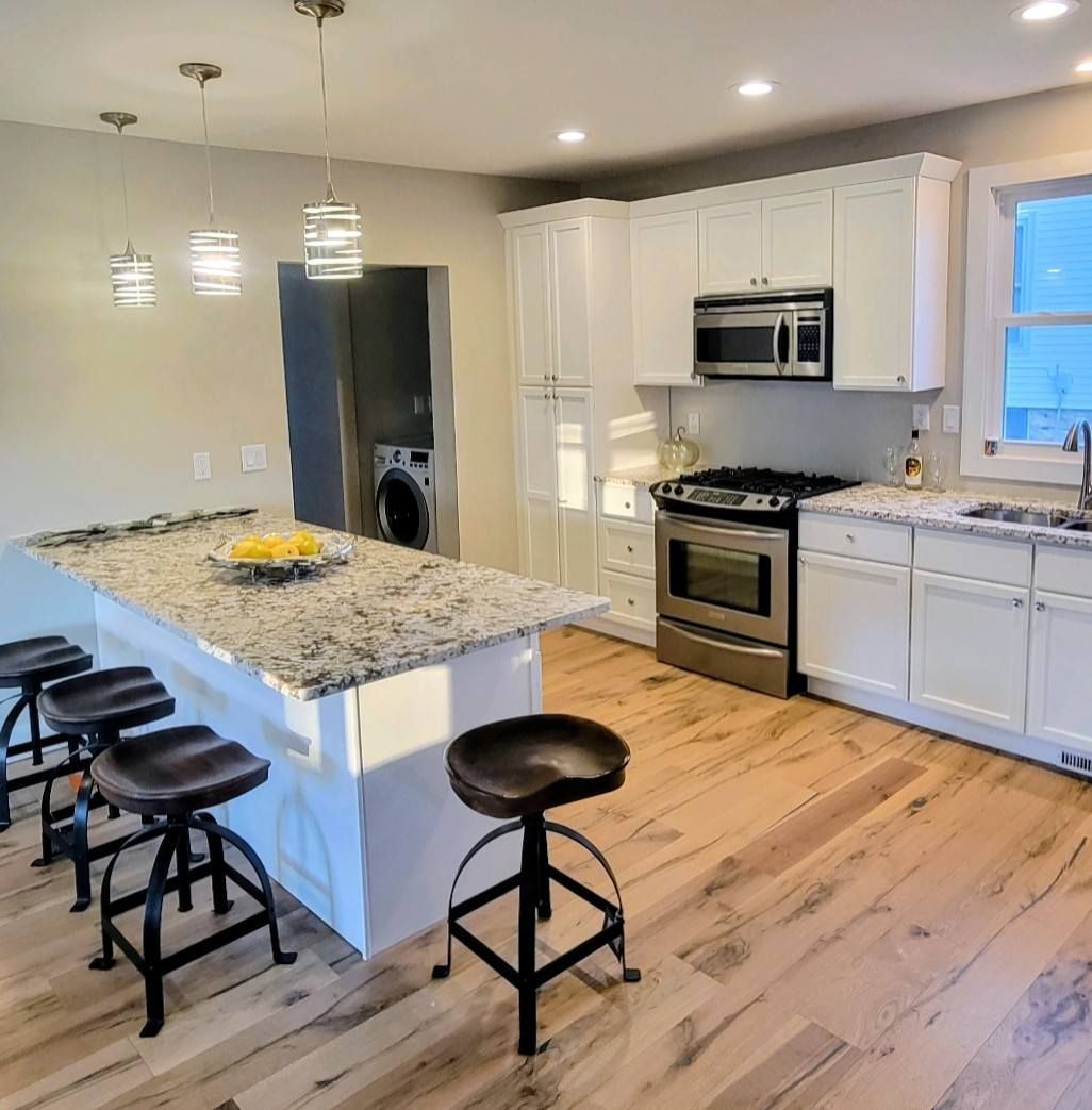 Bright modern kitchen with white cabinets, island, granite countertops, and black bar stools.