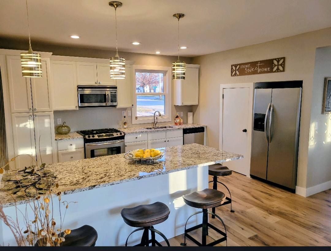 Bright modern kitchen with granite island, bar stools, stainless steel appliances, and hardwood floors