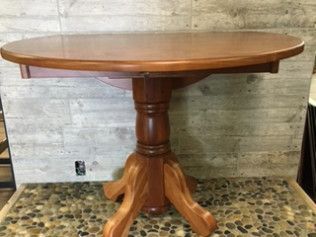 Round wooden pedestal table with a polished top and four curved legs on a patterned floor.