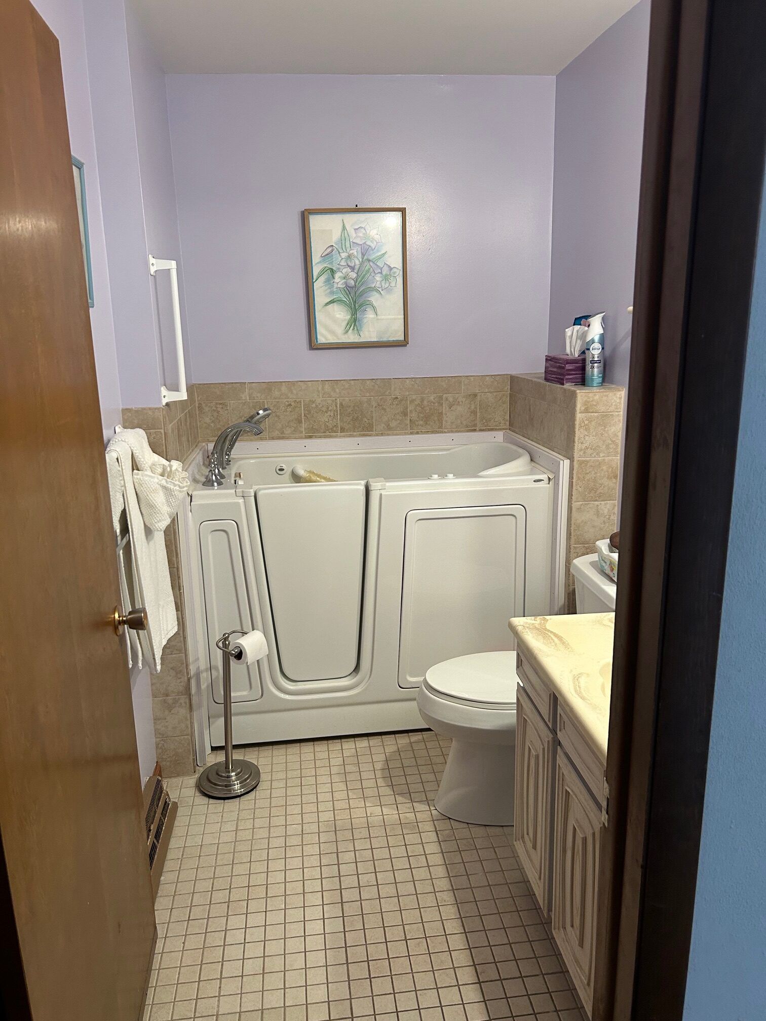Small bathroom with a walk-in tub, beige tile floor, lavender walls, and a framed picture.