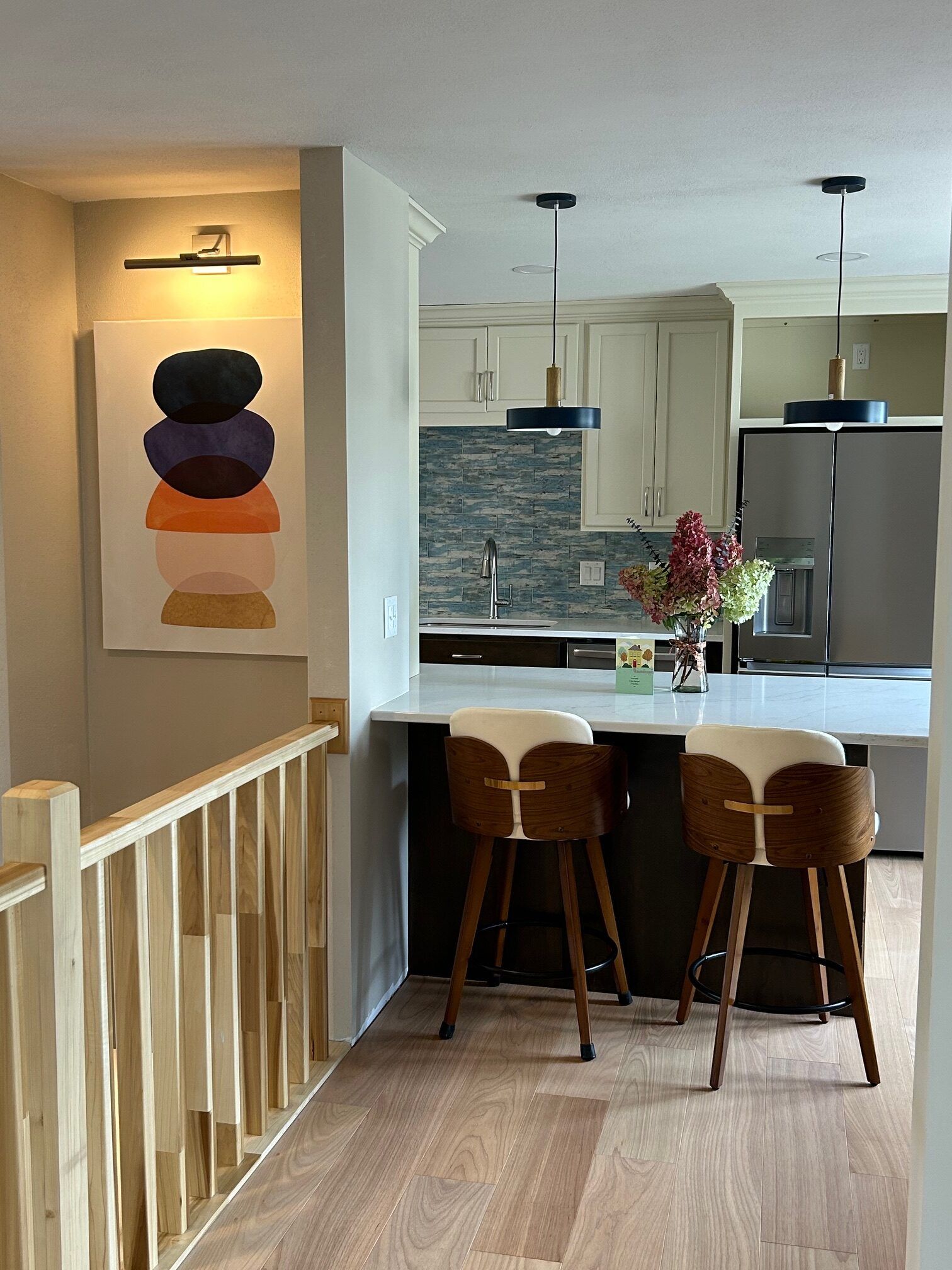 Bright hallway overlooking a modern kitchen with island, bar stools, and a floral centerpiece
