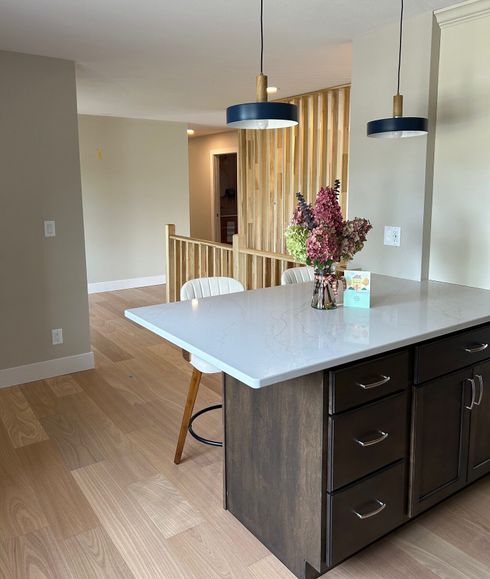 Modern kitchen with island, white countertop, dark cabinets, pendant lights, and a vase of flowers