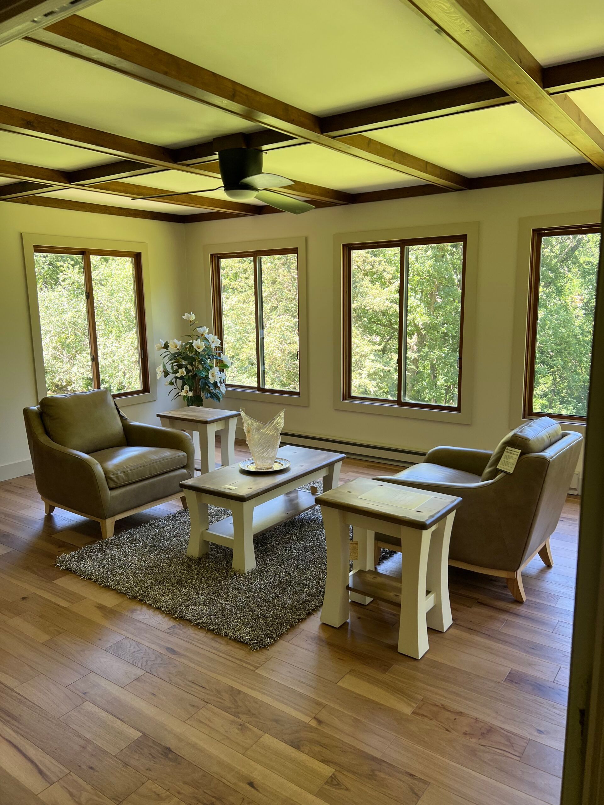 Cozy sunroom with wicker chairs, coffee table, rug, wood floor, and large windows overlooking trees